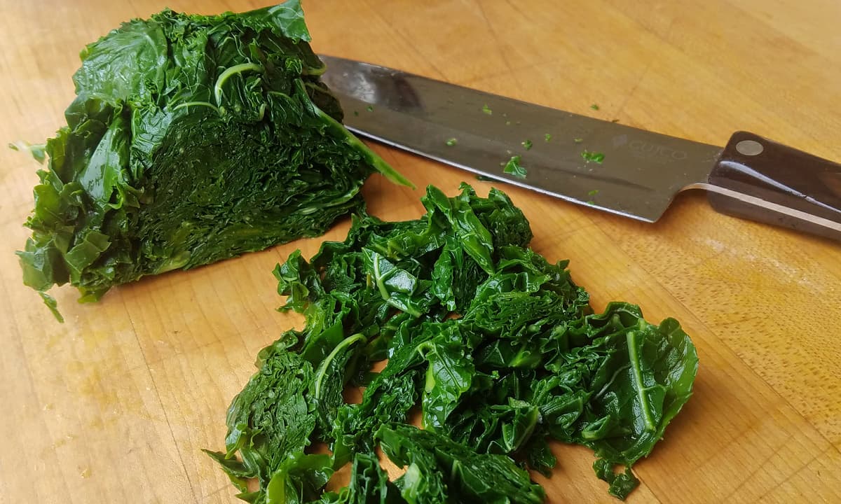 Wet, blanched kale on chopping board with knife.