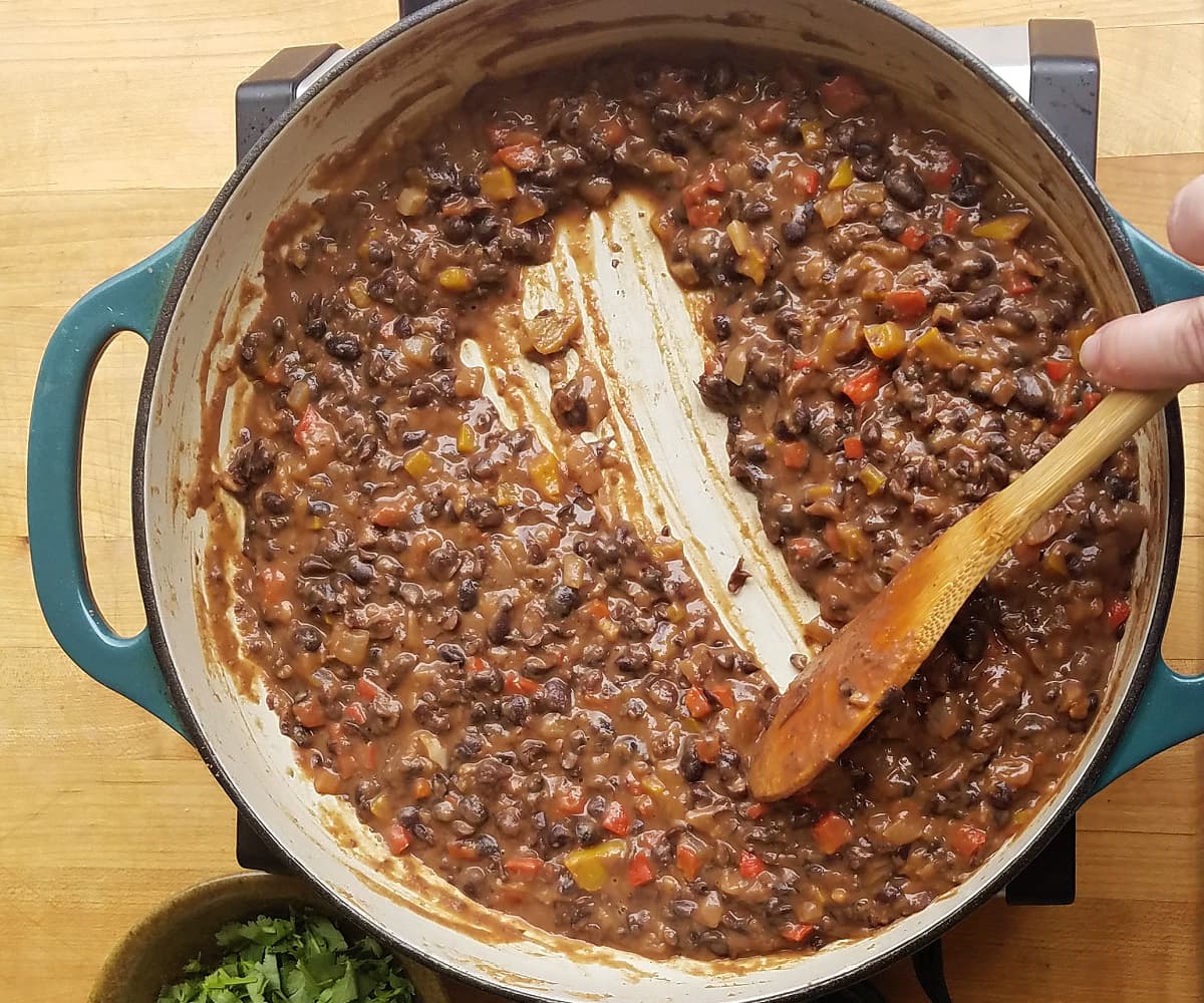 beans cooking in skillet, with a wooden spoon drawn acrosss to illustrate thickness of the beans.