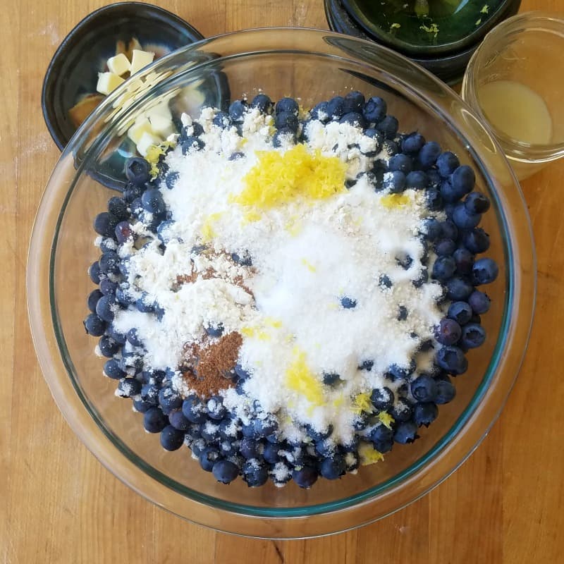 mixing blueberry pie ingredients in a glass mixing bowl
