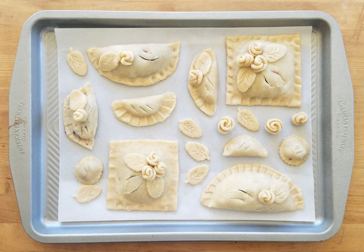 Baking tray with many small handpies made with sweet pie dough, each decorated with pie dough roses.