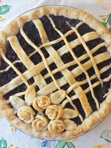 Freshly baked blueberry pie with lattice top adorned with pastry flowers.