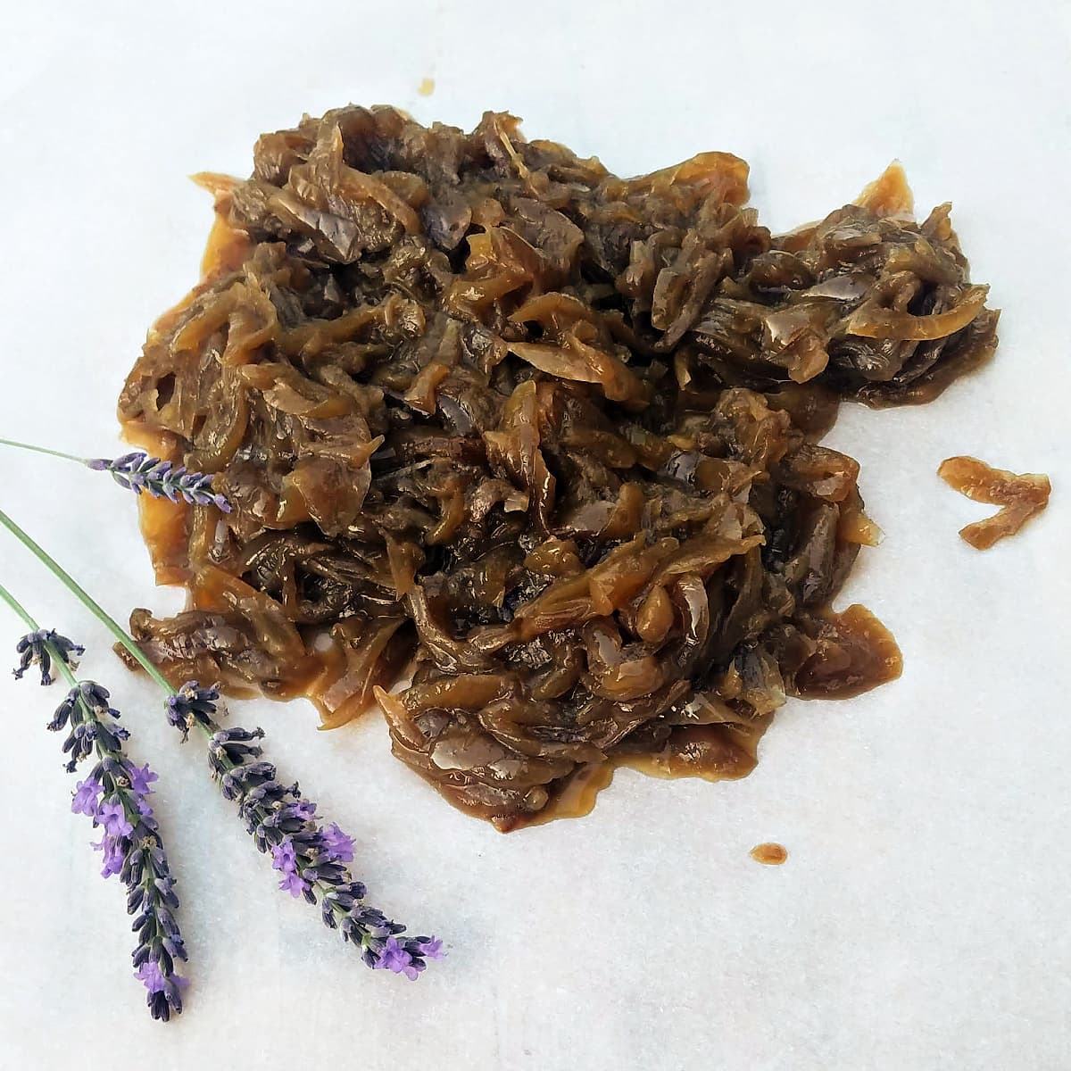 Caramelized onions on a sheet of parchment, with a frond of lavender on the side.