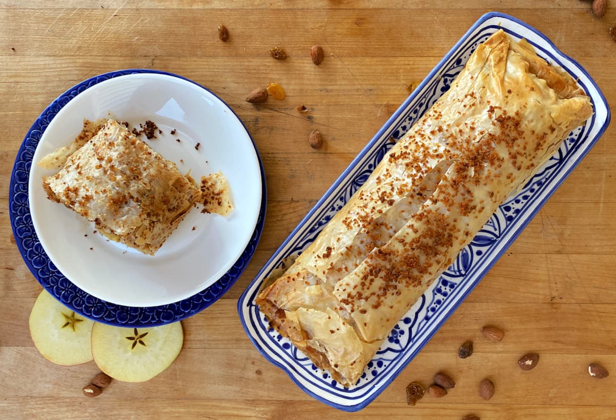 Whole apple strudel on long serving plate, and single serving on a small plate.