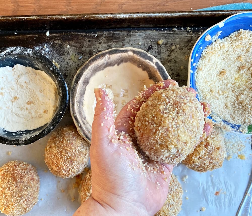 Breaded Scotch egg breaded sausage ball in palm of hand. 