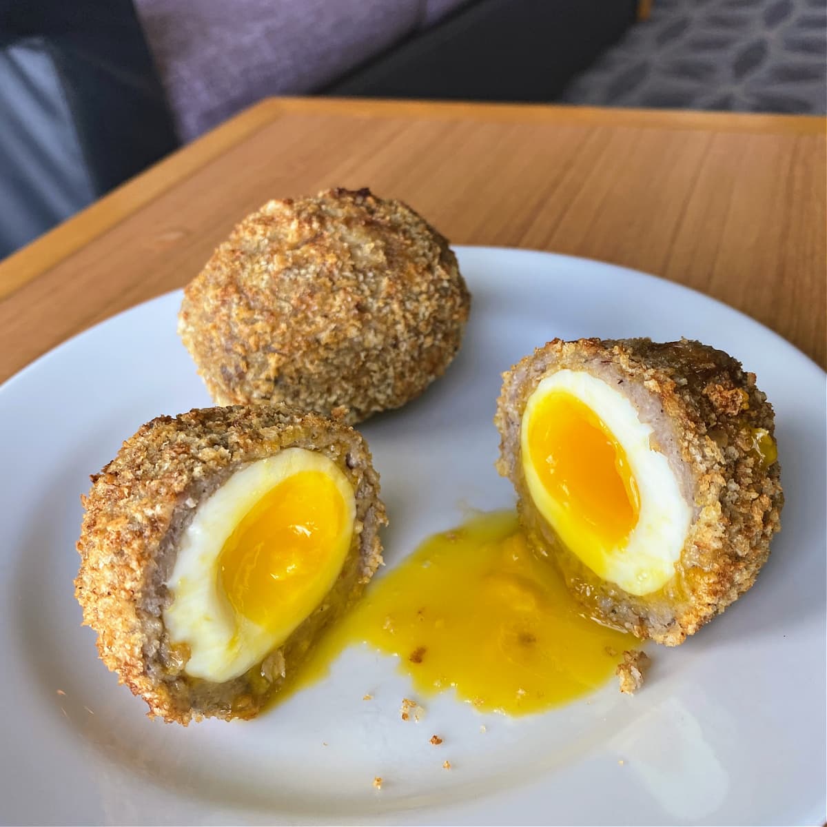 Scotch Eggs cut on a white plate, runny yolk spilling out. 