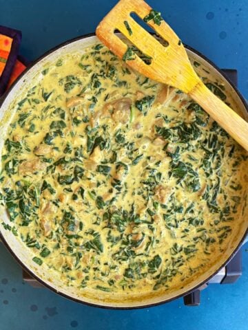Spinach and chicken in a thick, curry colored creamy sauce, in a large enameled skillet..