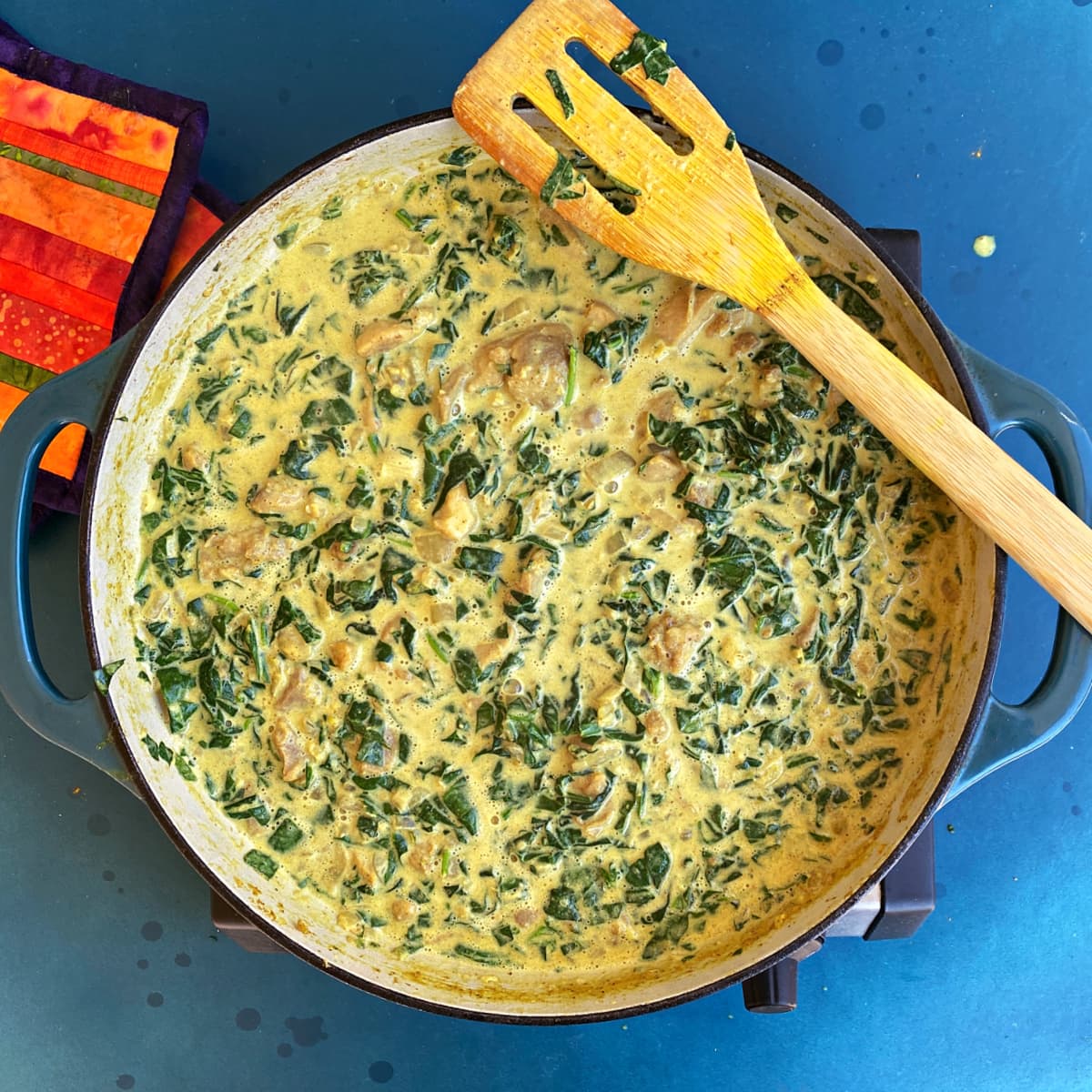 Spinach and chicken in a thick, curry colored creamy sauce, in a large enameled skillet.. 