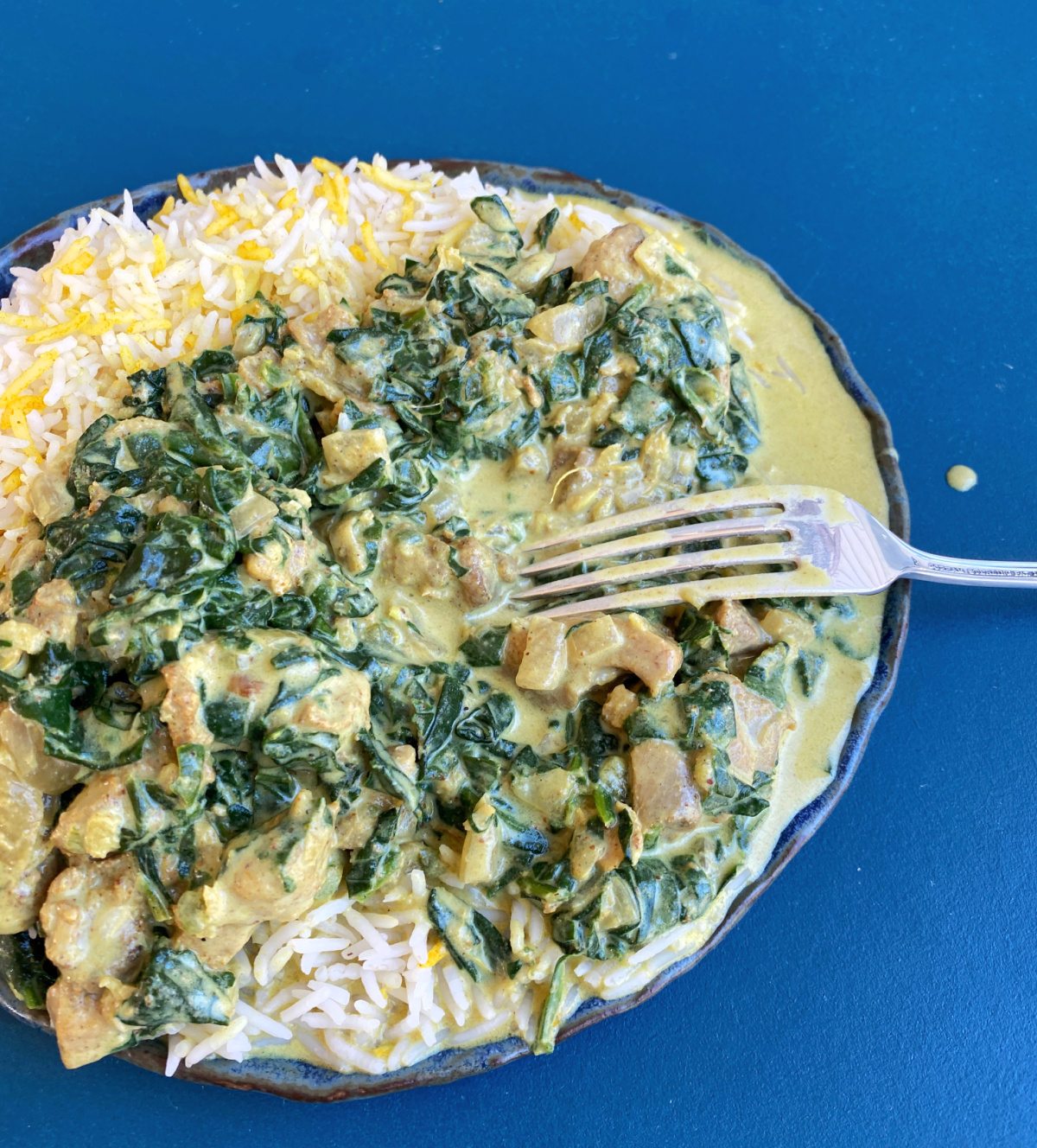 Chicken saag and turmeric rice, plated, with fork.