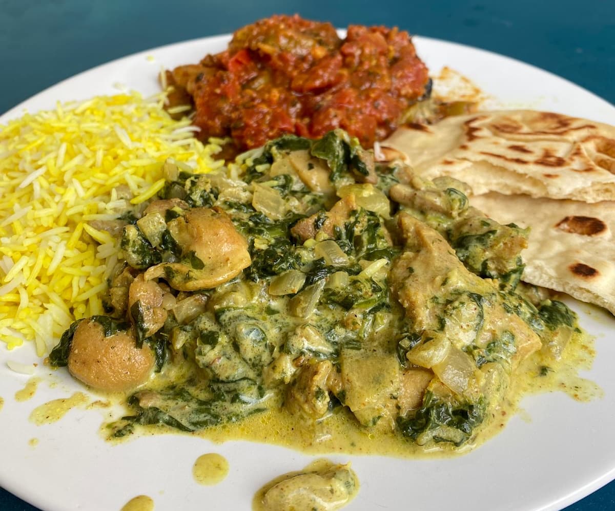 Chicken saag plated with turmeric rice, pickled eggplant, and naan. 