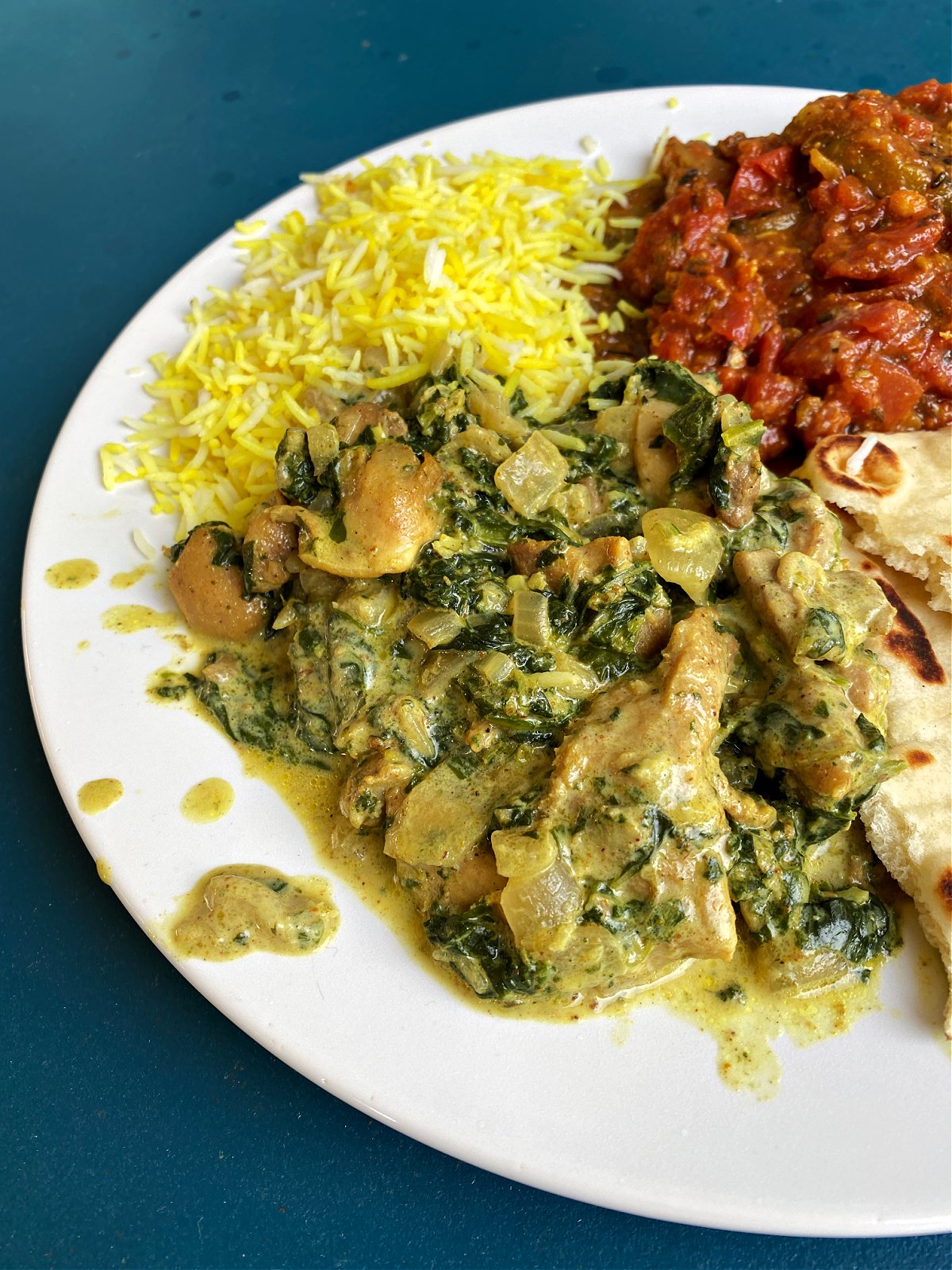Spinach chicken plated with rice, eggplant, and naan. 