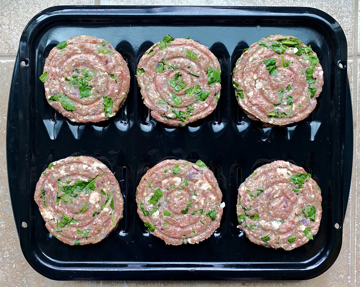 Uncooked burgers on black broiler tray. 