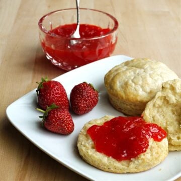Two biscuits on a plate. One sliced open and spread with strawberry jam.