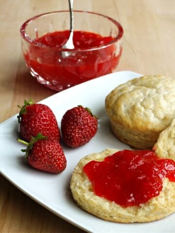 Two biscuits on a plate. One sliced open and spread with strawberry jam.