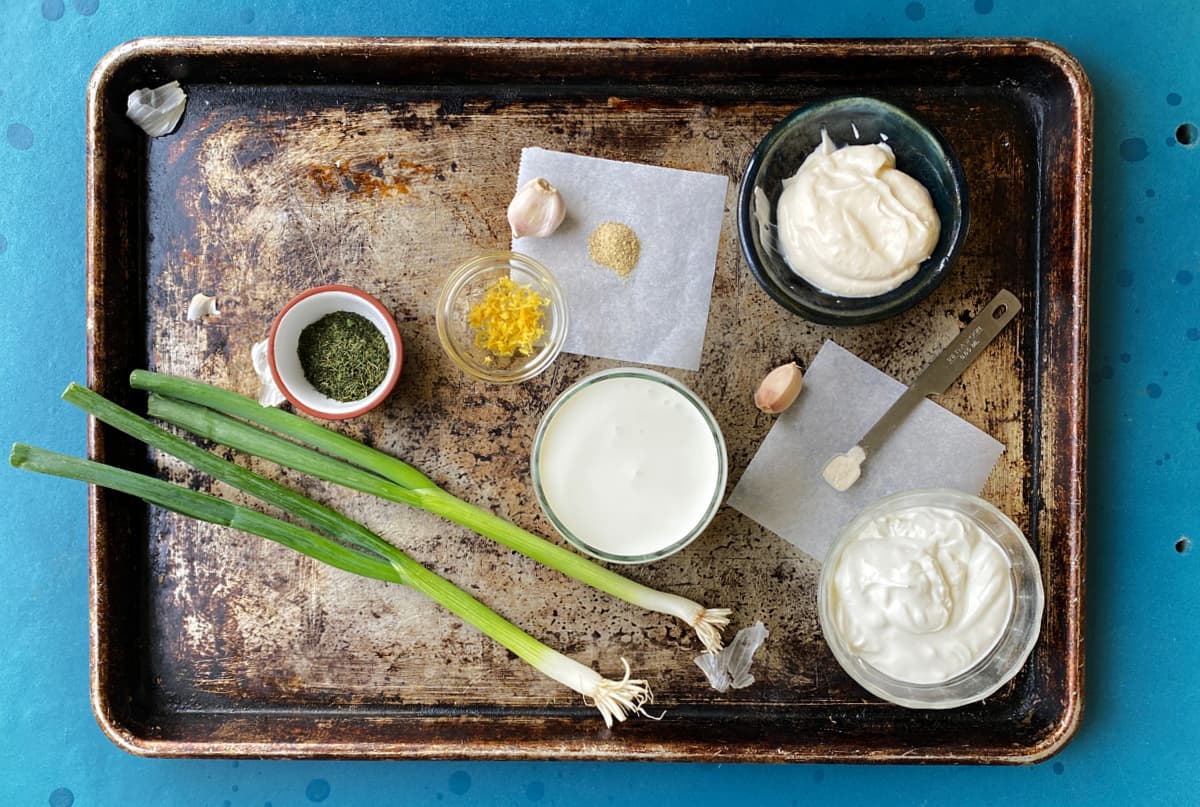 Buttermilk dressing ingredients on a baking tray: Buttermilk, sour cream, mayo, green onions, dill, garlic, lemon zest, white pepper, chili powder, xanthan gum. 