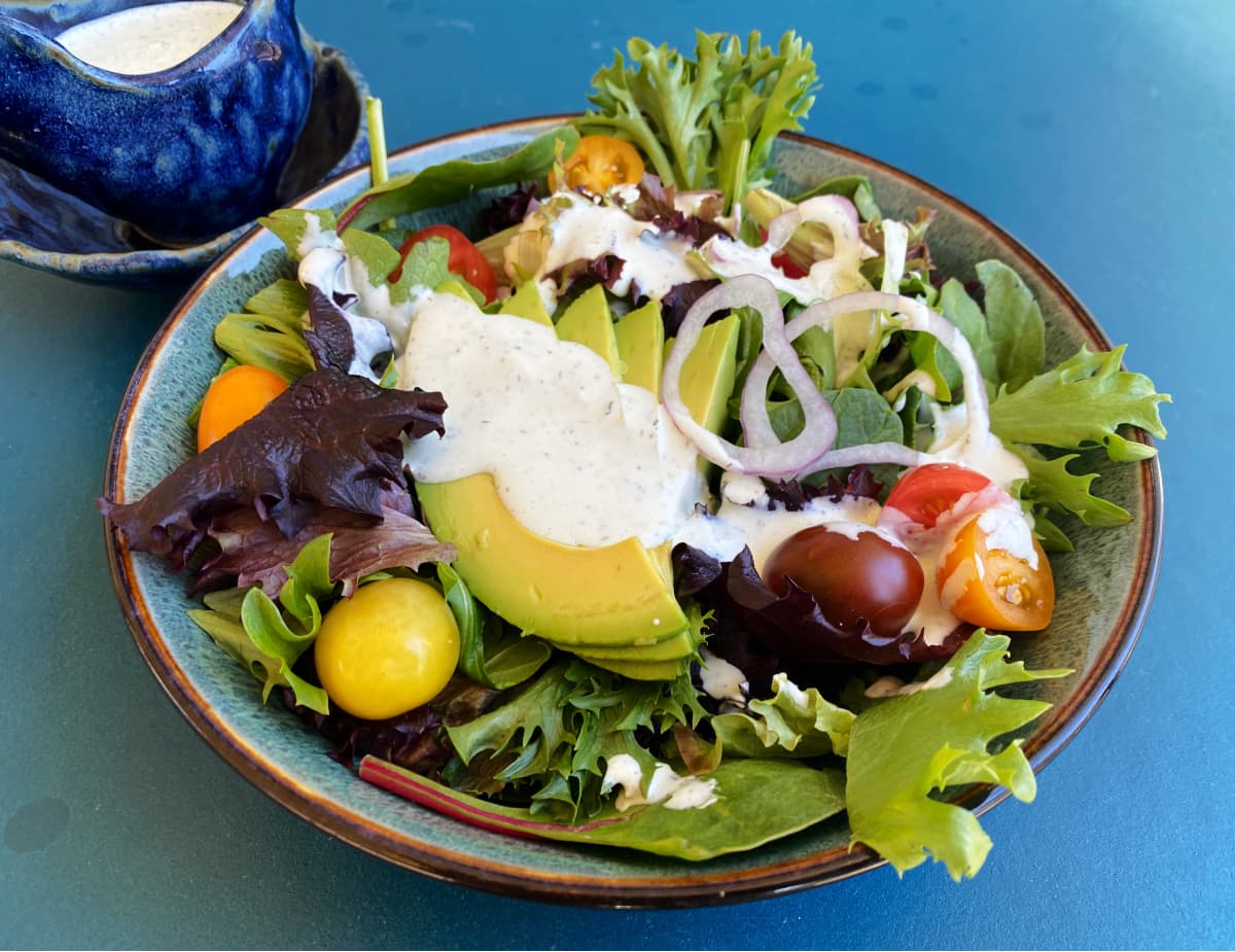 Green salad on plate, with tomatoes, avocado, and topped with fresh ranch dressing.