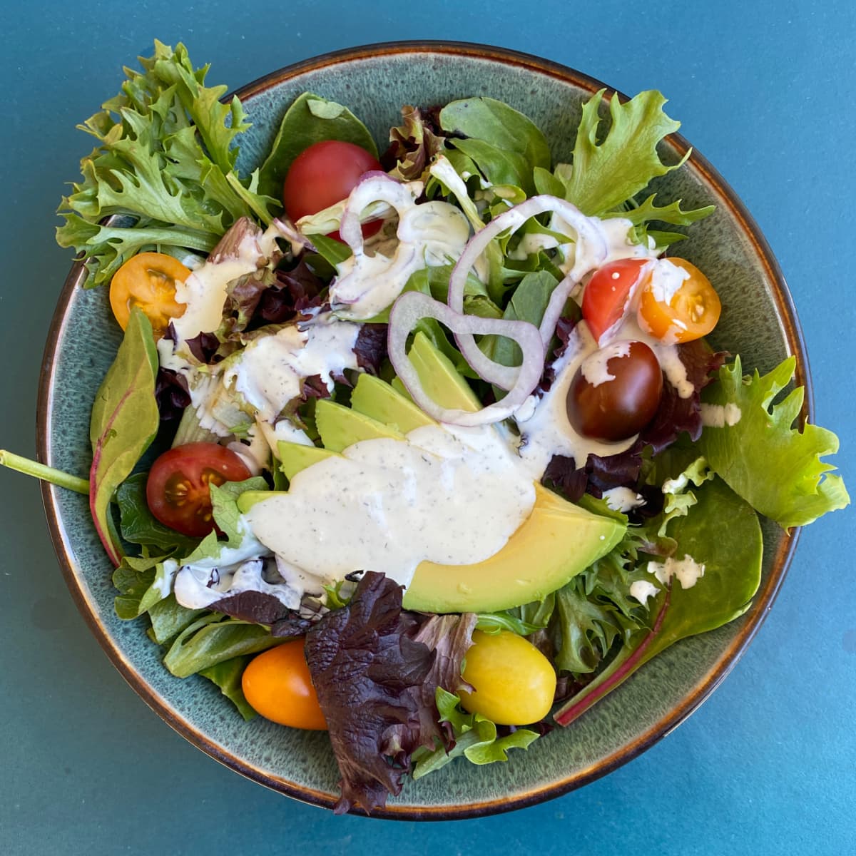 Green salad on plate, with tomatoes, avocado, and topped with fresh ranch dressing. 