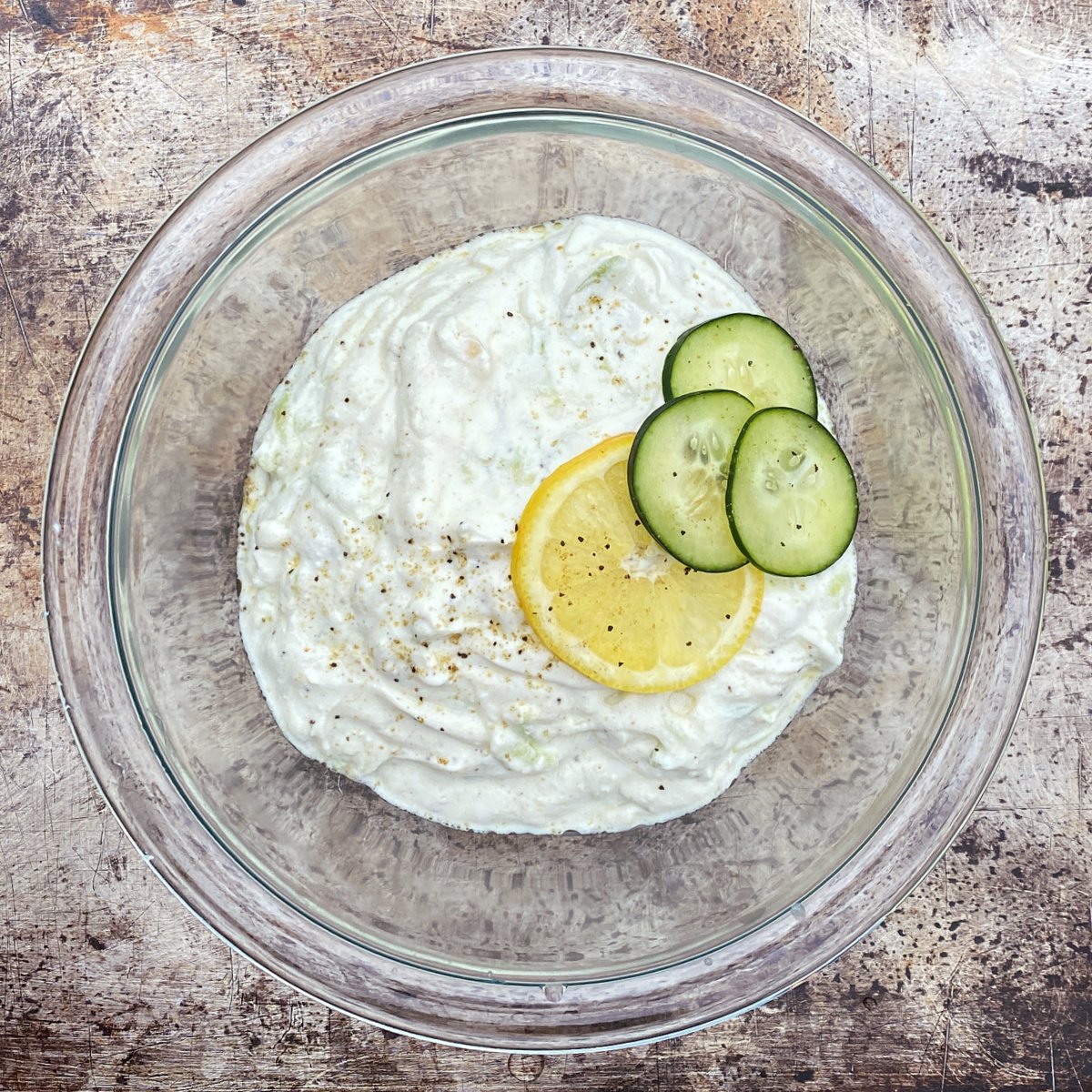 Prepared tzadiki in a glass bowl, garnished with cucumber and lemon slices. 