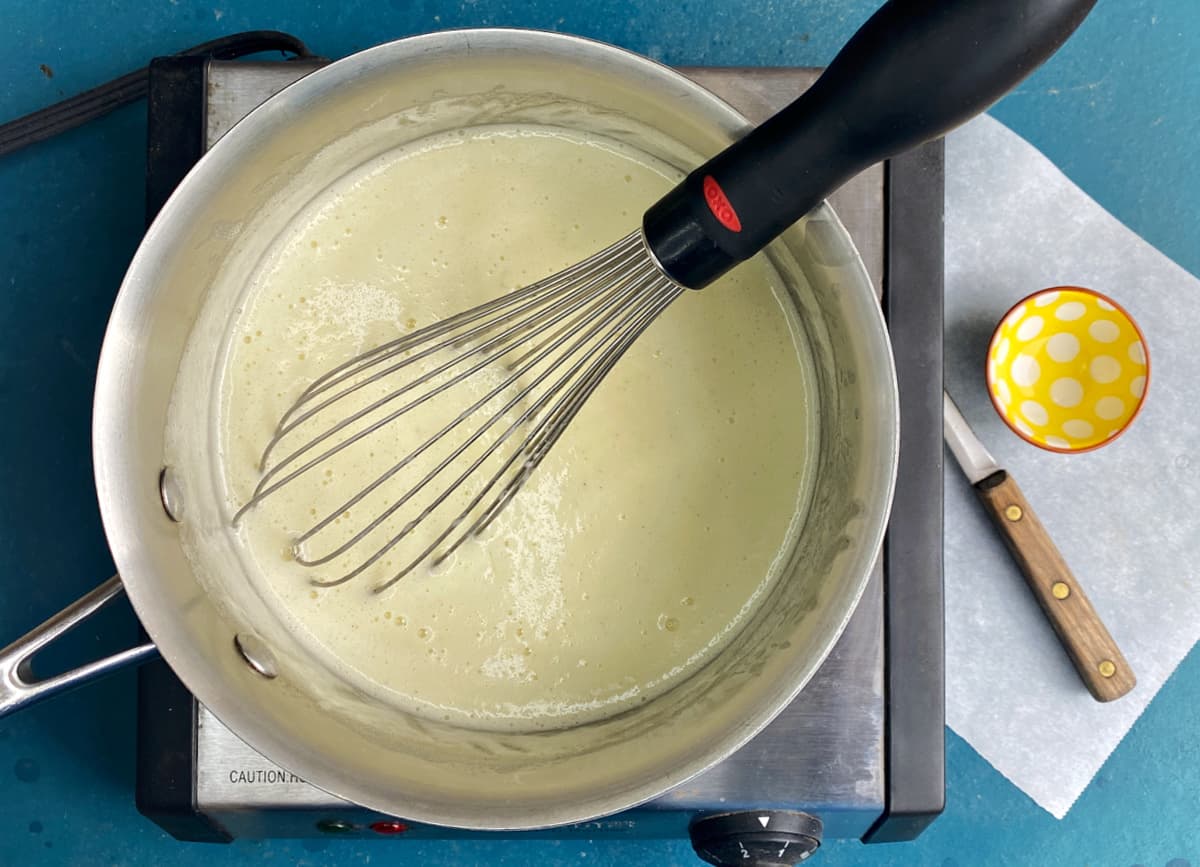 Cooked custard for ice cream in a saucepan, with a whisk.
