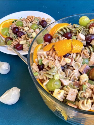 Large glass serving bowl filled with a mix of spiral pasta, cubed turkey, grapes, celery, and other ingredients.