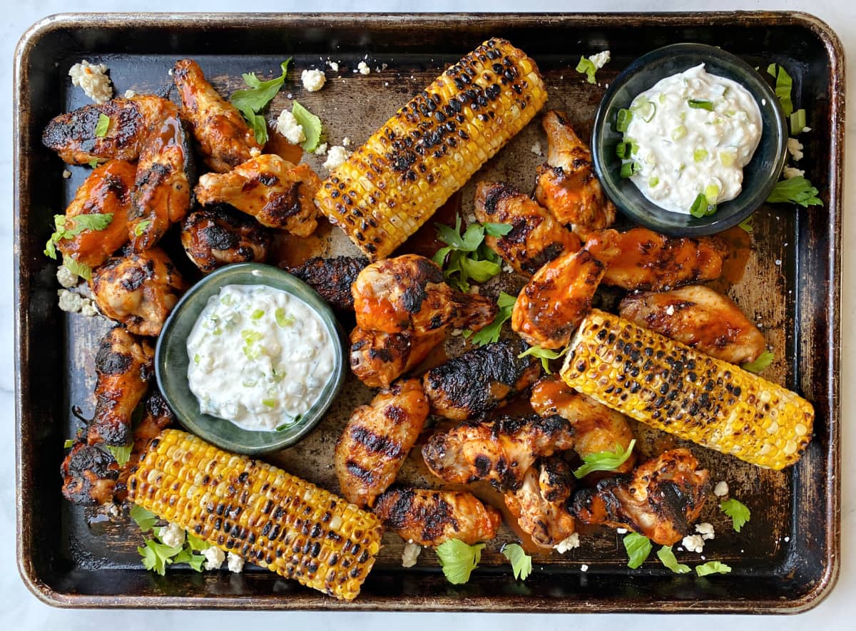 grilled corn, buffalo wings, and blue cheese sauce served on an old baking tray.