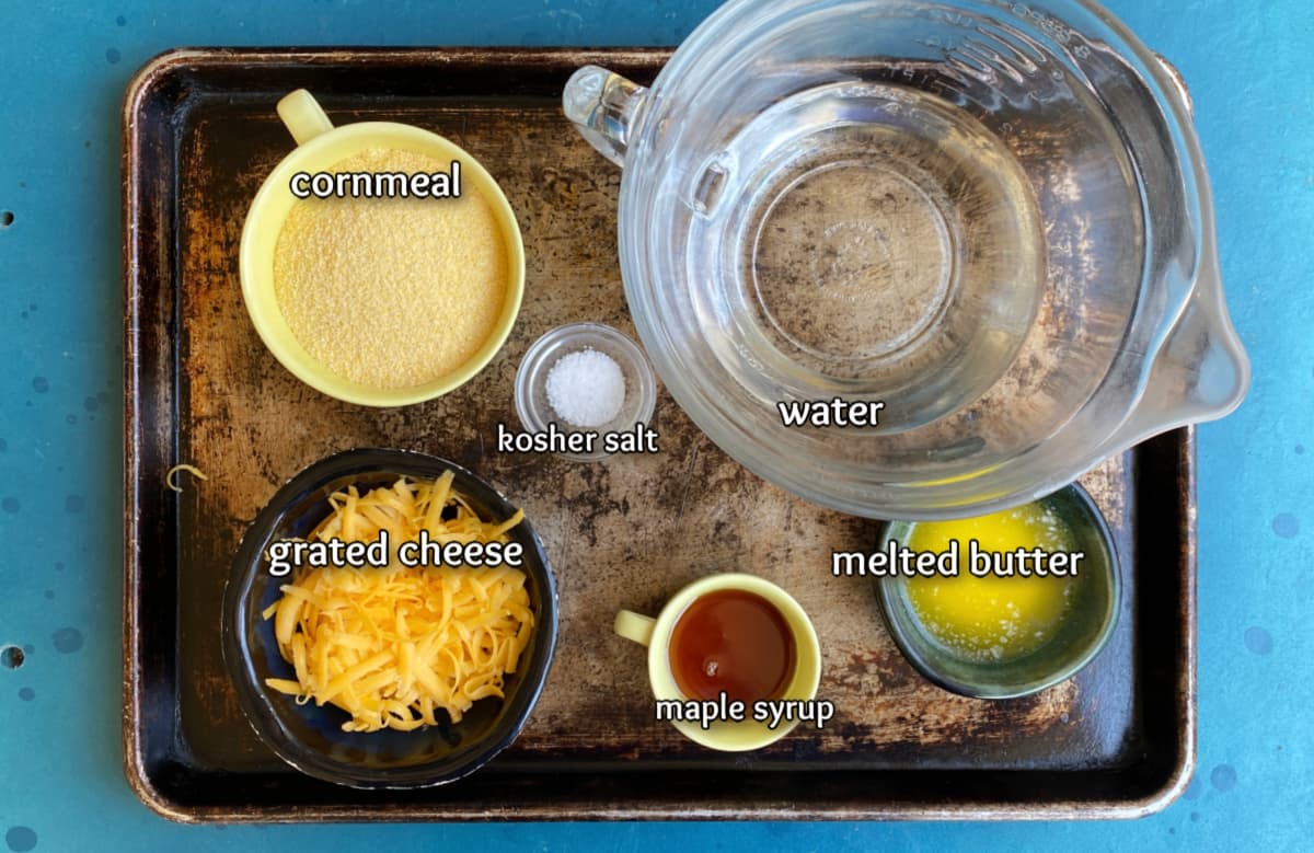 Ingredients for cheesy polenta topping in small bowls, resting on sheet pan. 