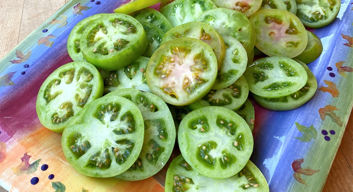 Sliced green tomatoes on a decorative rectangular tray. 