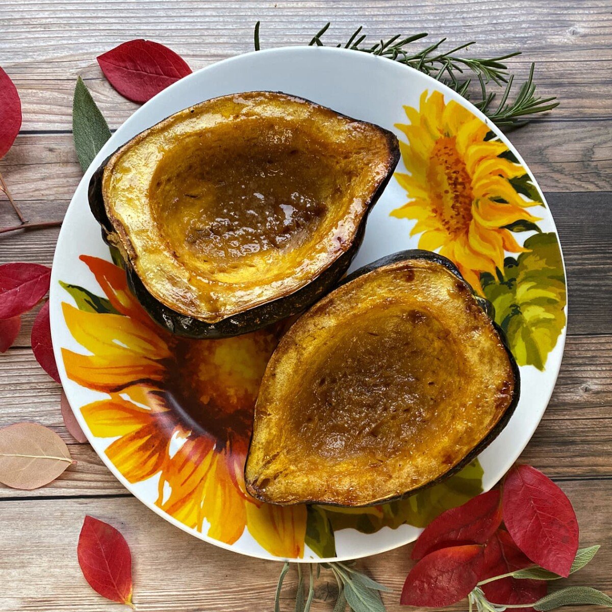 Two halves of a roasted acorn squash facing up on a plate decorated with sunflowers. 