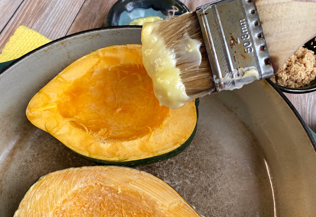 Paint brush loaded with softened butter, hovering over cut acorn squash half.