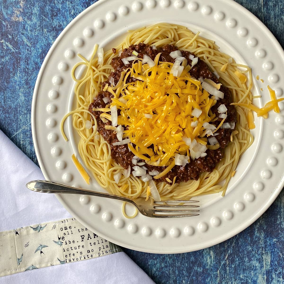 Close-up of chili and spaghetti on a white plate, topped with onions and cheese. 