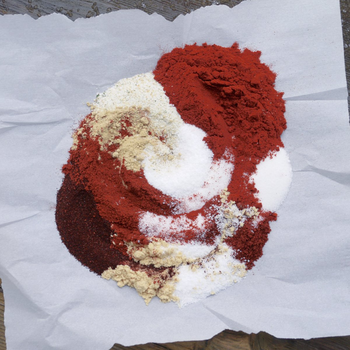 Top view of colorful spices whirled on a torn piece of parchment paper. 