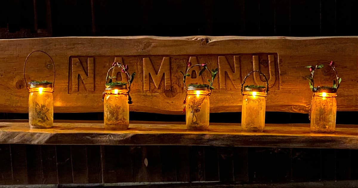Five fairy lanterns on a rustic bench, with the word "NAMANU" carved in the back of the bench. (Camp Namanu, 2021)
