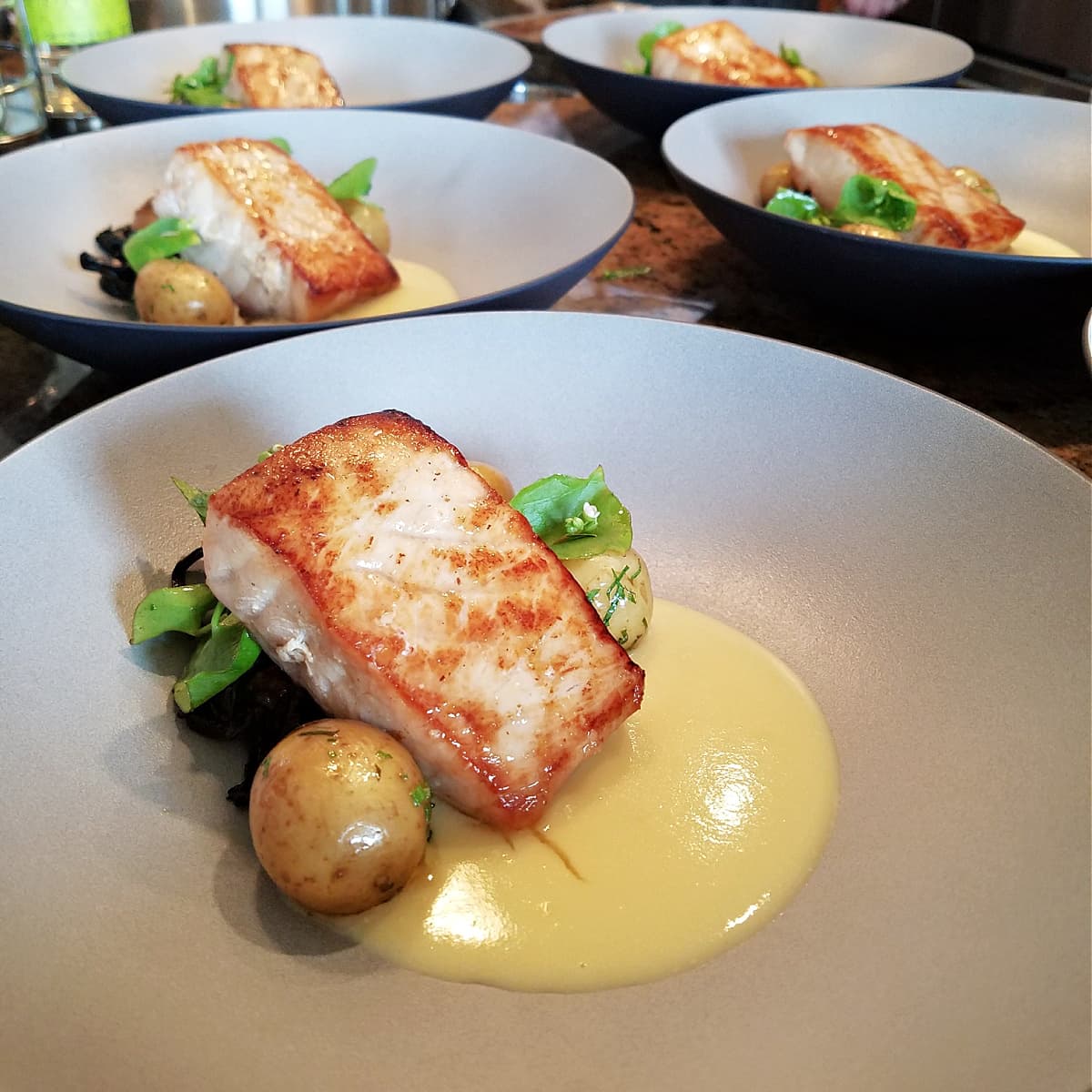 Pan-Seared Sturgeon fillet laying on a bed of greens, baby potatoes, and a creamy yellow sauce. 