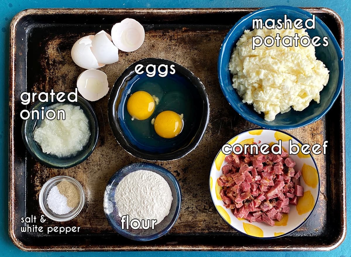 Ingredients for making mashed poato pancakes, displayed and labeled on old baking tray.