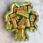 Shamrock shaped ceramic dish filled with bar cuts of layered jello. Colors green, orange, and yellow.