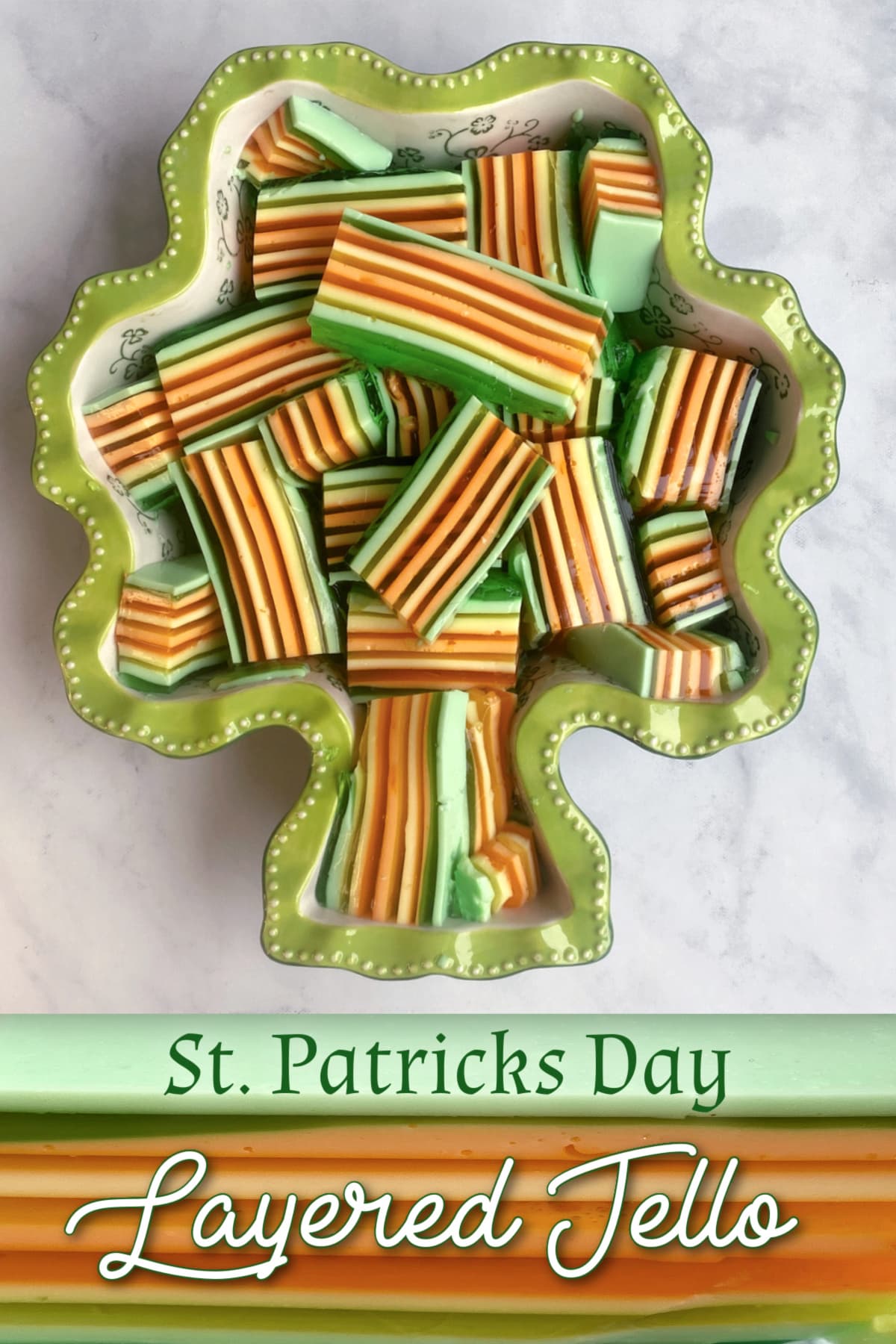 Shamrock shaped ceramic dish filled with bar cuts of layered jello. Colors green, orange, and yellow. Pin text reads, St Patrick's Day Layered Jello.