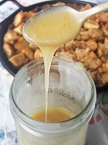 Whiskey sauce pouring from spoon into a jar. Bread pudding in the background.