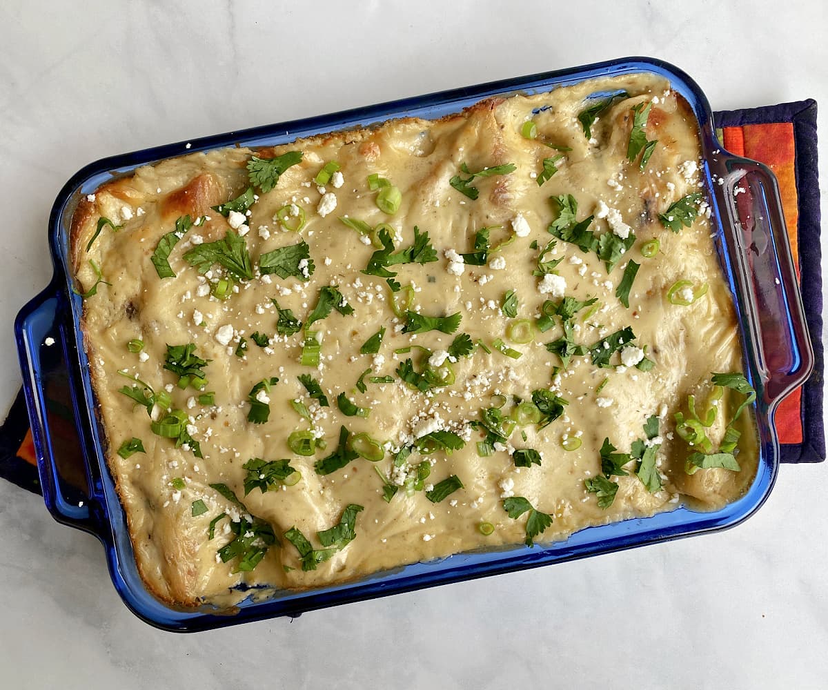 Baked seafood enchiladas in a blue casserole dish, garnished with cilantro, green onions, and cotija.