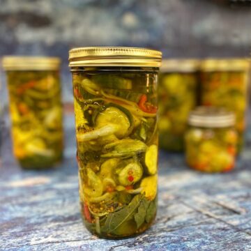 Four Bread & Butter Pickles in jars on a blue counter, after processing.