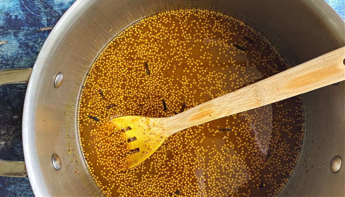 Overhead shot of pickling syrup, with many mustard seeds floating on top.