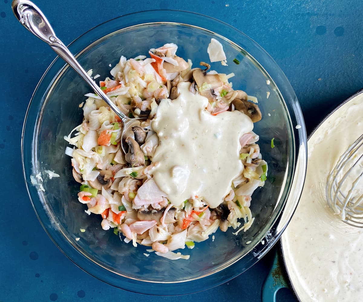 Sauce added to seafood filling mixture in glass mixing bowl.