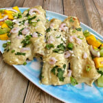 Four seafood enchiladas on a long platter, garnished with bay shrimp, cilantro, and cotija. Mango salad on the side.