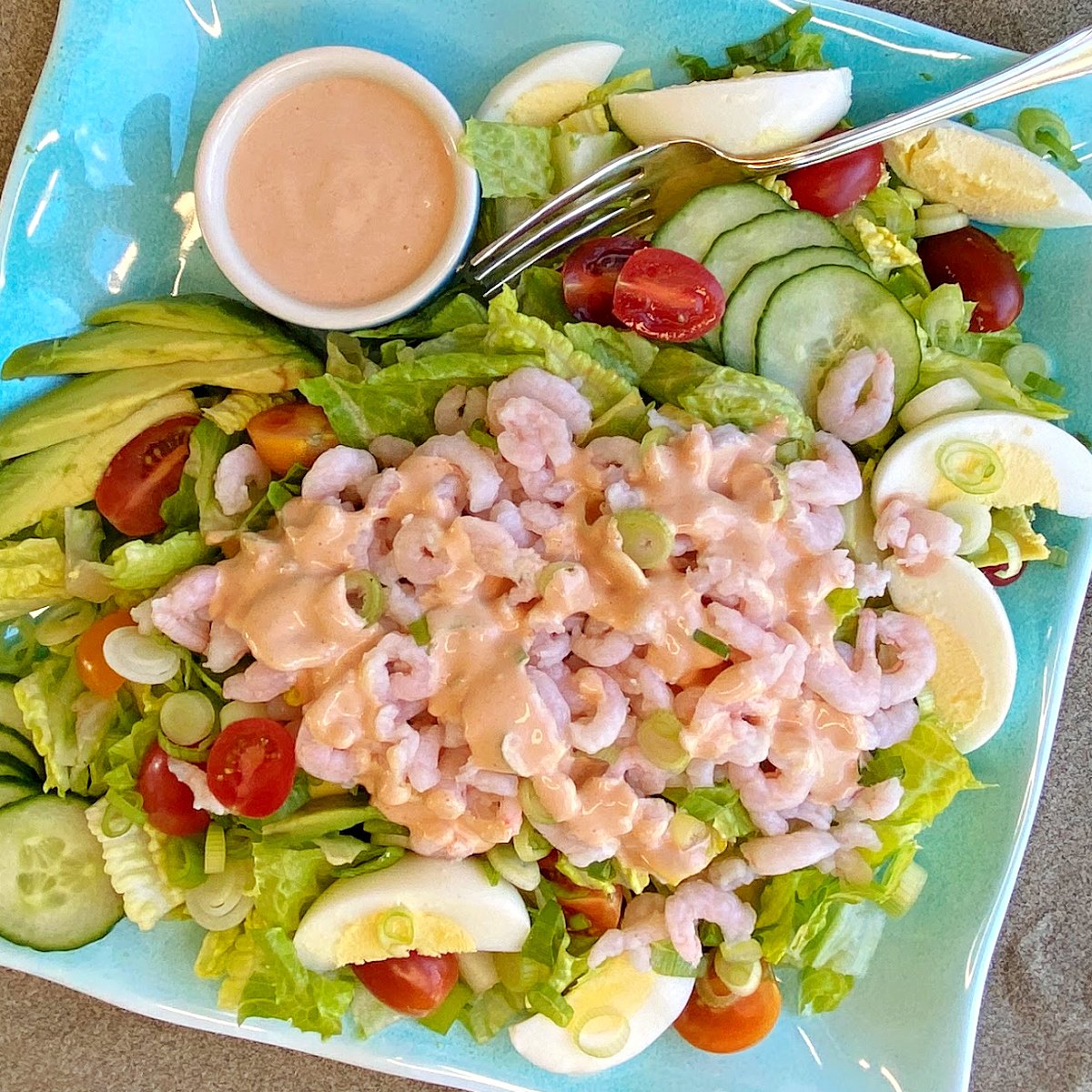 Overhead shot of Shrimp Louie salad assembled on a plate with dressing, and more dressing on the side in a small service cup.