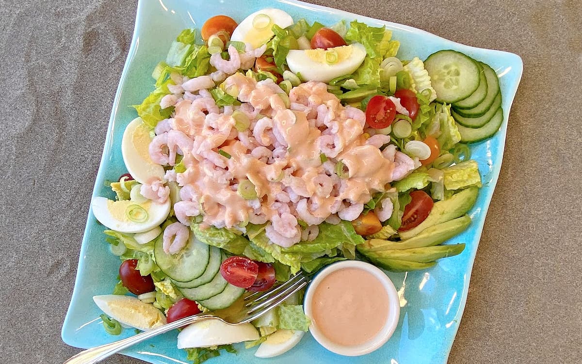 Shrimp Louie assembled on a plate with dressing, and more dressing on the side in a small service cup.