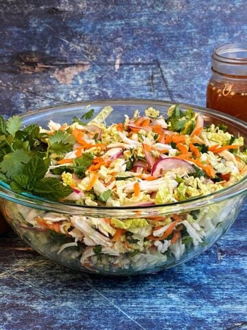 Vietnamese chicken salad in large glass serving bowl, with a jar of nuoc cham behind and salad tongs to the left.