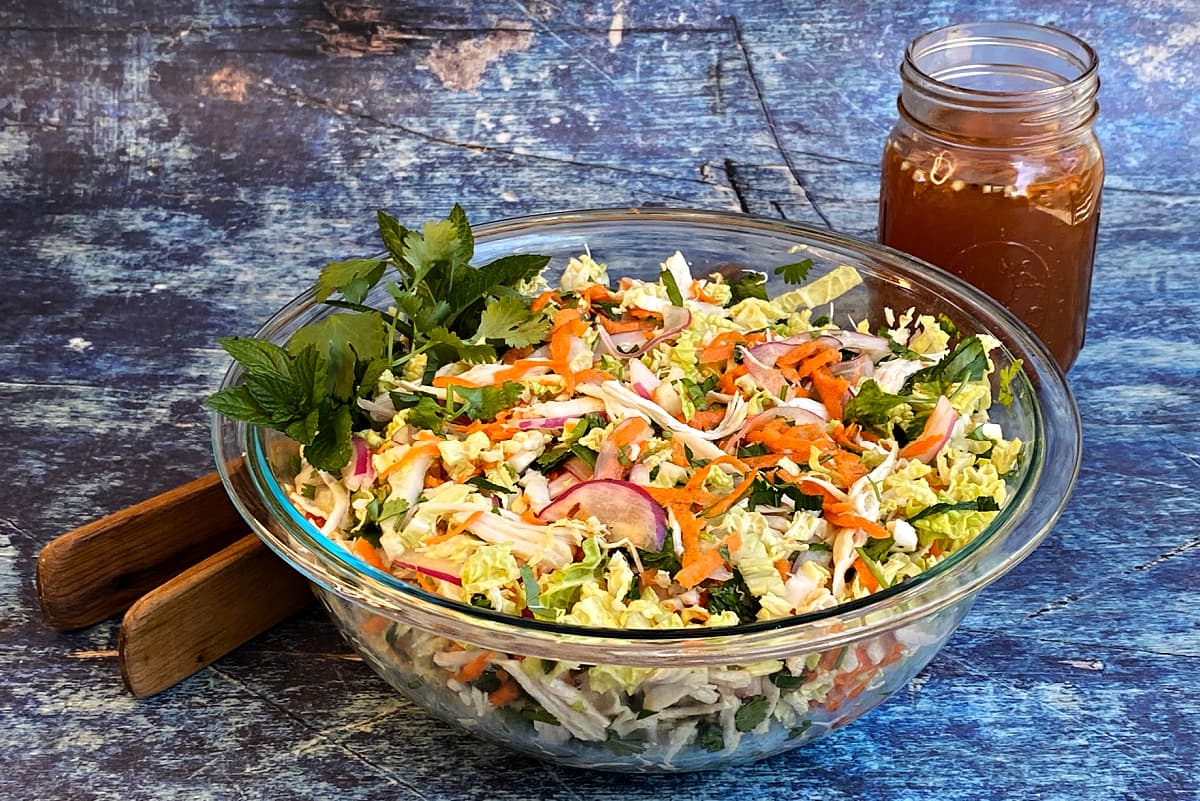 Vietnamese chicken salad in large glass serving bowl, with a jar of nuoc cham behind and salad tongs to the left.