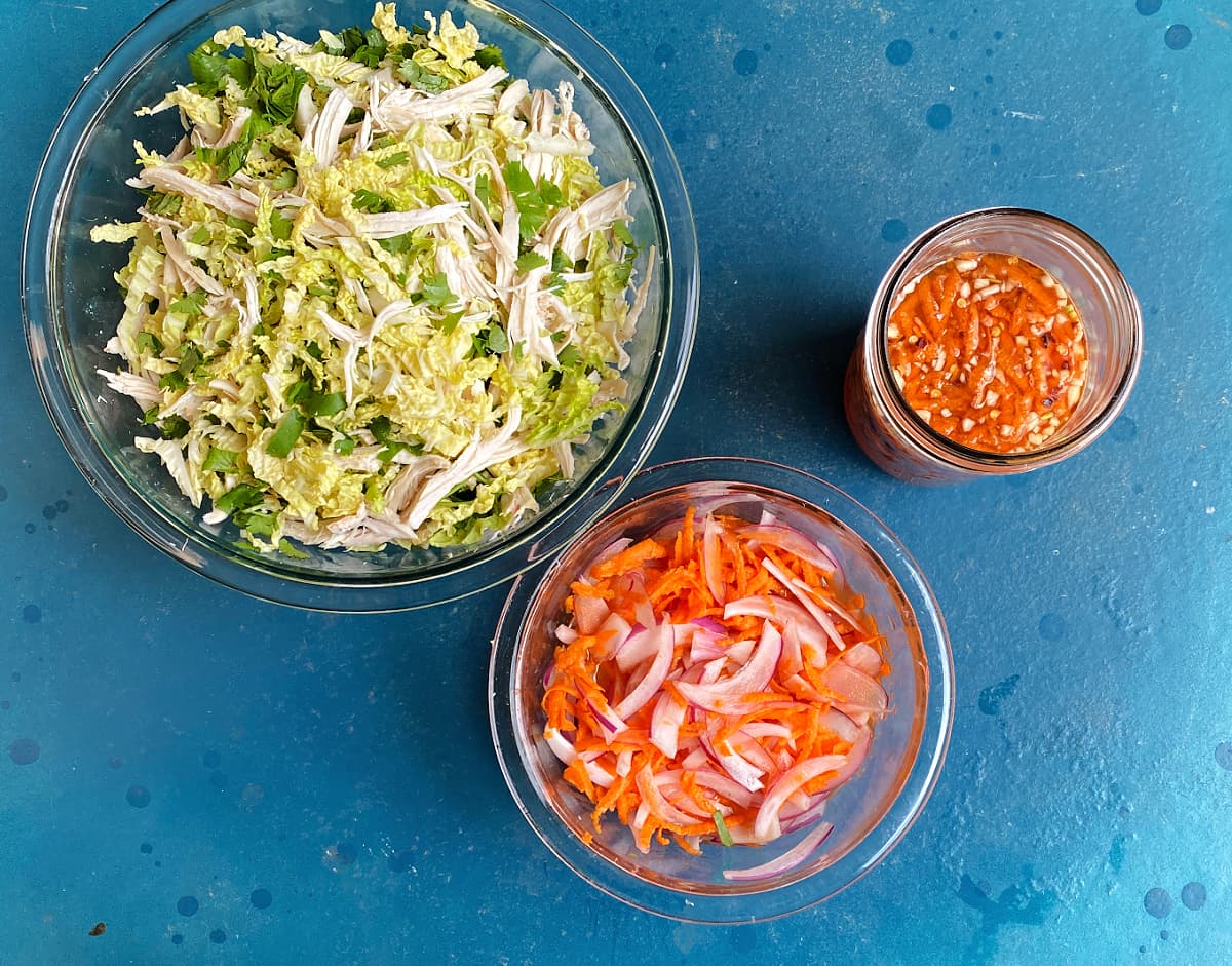 two glass mixing bowls; one with chicken and cabbages tossed, the other with marinating onions and carrots.