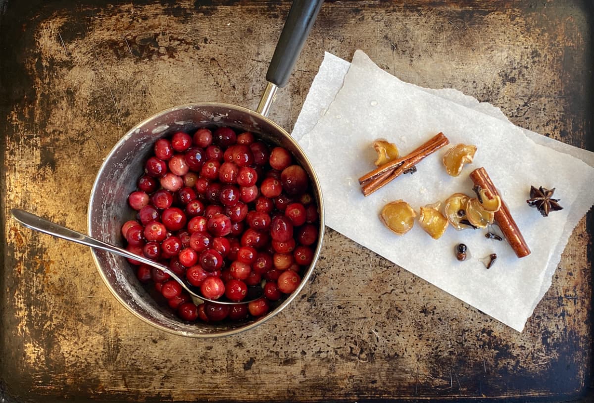 Small saucepan half full of cranberries, with discarded whole spices on a piece of parchment on the side.