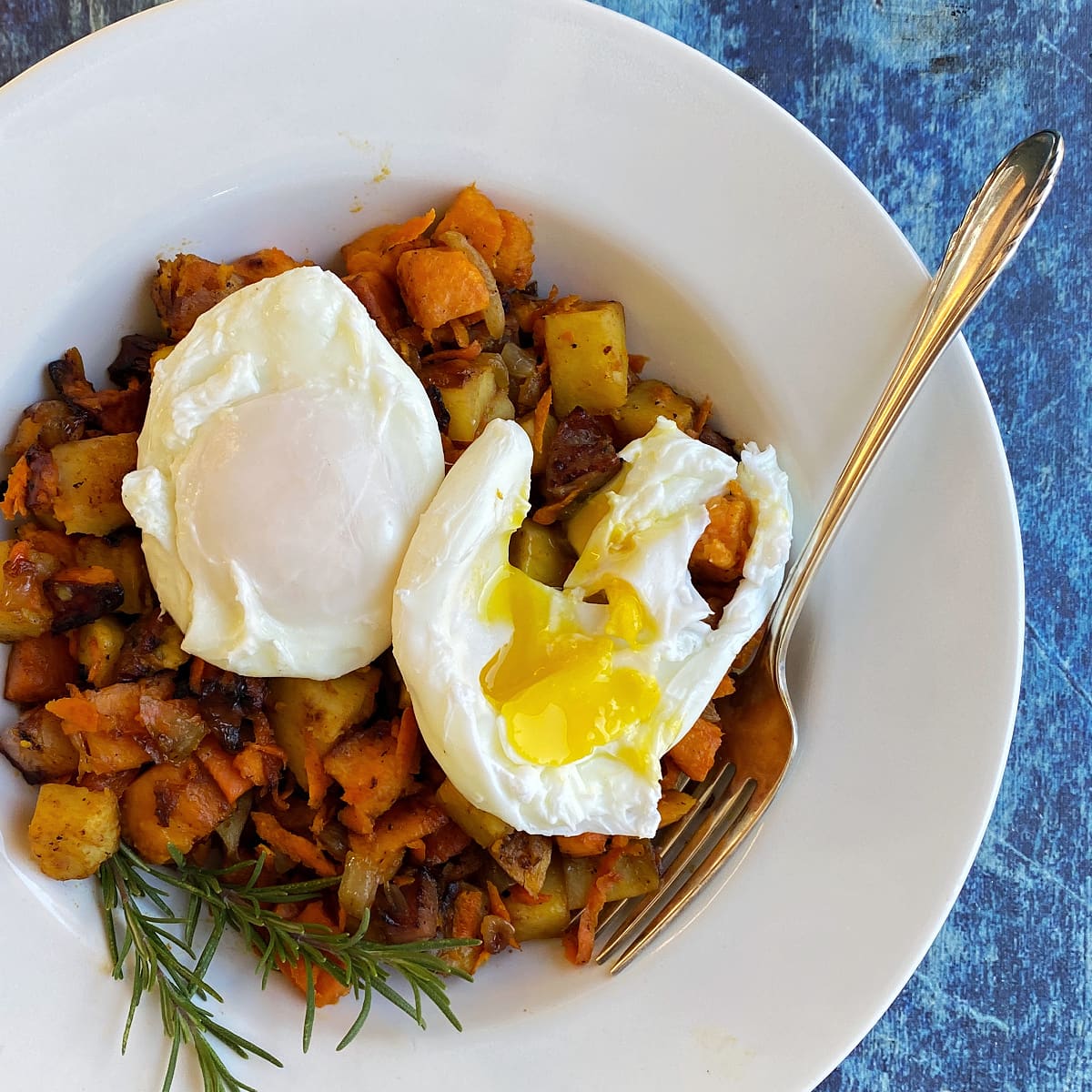 Overhead shot of a bowl of sweet potato hash with two poached eggs on top. One egg yolk is broken and runny..