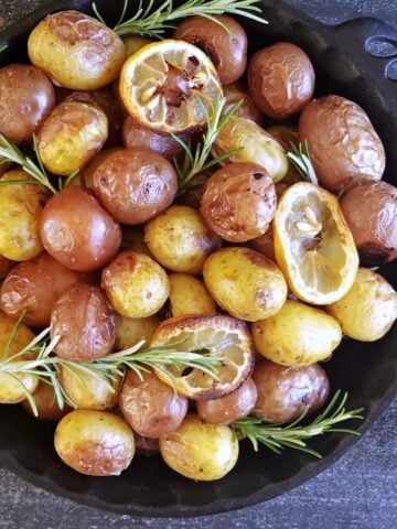 Overhead shot of cast iron pie dish filled with roasted baby potatoes and lemon slices, garnished with fresh rosemary.