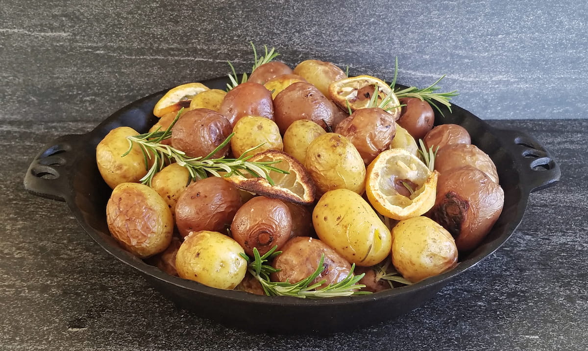 Cast iron pie dish filled with roasted baby potatoes and lemon slices, garnished with fresh rosemary.